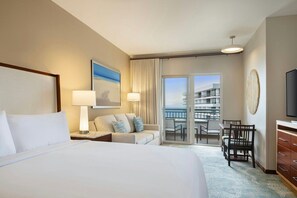 Habitación de hotel con una cama grande, un sofá, una mesa de comedor con sillas, un televisor y un balcón con vistas.