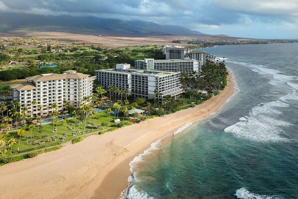 Un hotel frente a la playa con varias edificaciones, una playa de arena y vista al océano.