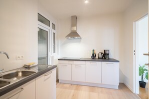 Een moderne keuken met een roestvrijstalen spoelbak, een inbouwoven, een afzuigkap en een aanrecht met een koffiezetapparaat.