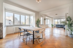 A spacious living area with a large wooden table and chairs, a sofa, and potted plants. - Modern 3-bedroom Apartment for Families (Antwerp)