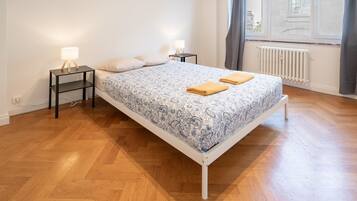 A bedroom with a bed, two bedside tables, a radiator, and a window with curtains.