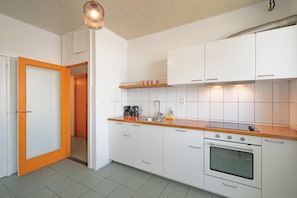 Uma cozinha moderna com armários brancos, bancada de madeira, forno embutido e luminária pendente.