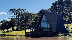 Una moderna casa flotante con techo triangular, ubicada sobre aguas tranquilas, rodeada de exuberante vegetación y árboles.