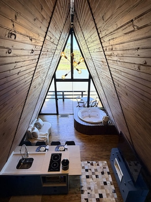 A cozy, triangular wooden interior with a dining area, a seating area with a hot tub, and a view of the outdoors.