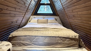 A triangular attic bedroom with a bed, a nightstand, and a window. - Lake cabin with hot tub and mountain views (Bom Jardim da Serra)