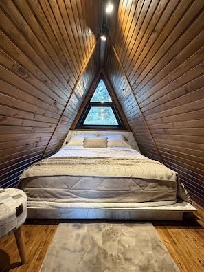 Ein schrägwandiges Schlafzimmer im Dachgeschoss mit einem Bett, einem Nachttisch und einem Fenster.