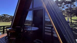 A modern, triangular-shaped cabin with a glass facade, a wooden deck, and a hot tub. - Lake cabin with hot tub and mountain views (Bom Jardim da Serra)