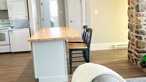 A modern kitchen with white appliances, a dining area with a wooden table and chairs, and a stone accent wall.
