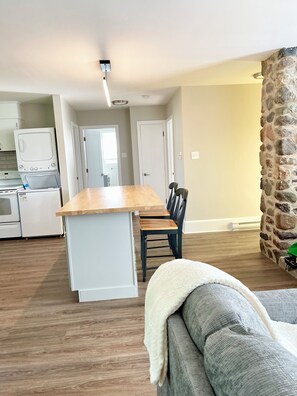 A modern kitchen with white appliances, a dining area with a wooden table and chairs, and a stone accent wall.
