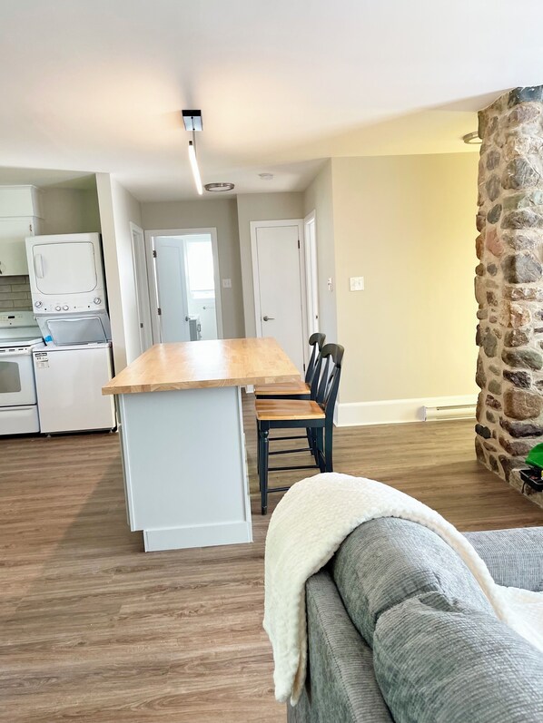 A modern kitchen with white appliances, a dining area with a wooden table and chairs, and a stone accent wall.