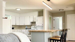A modern kitchen with white cabinets, a built-in oven, and a microwave. There is a dining area with a wooden table and black chairs.
