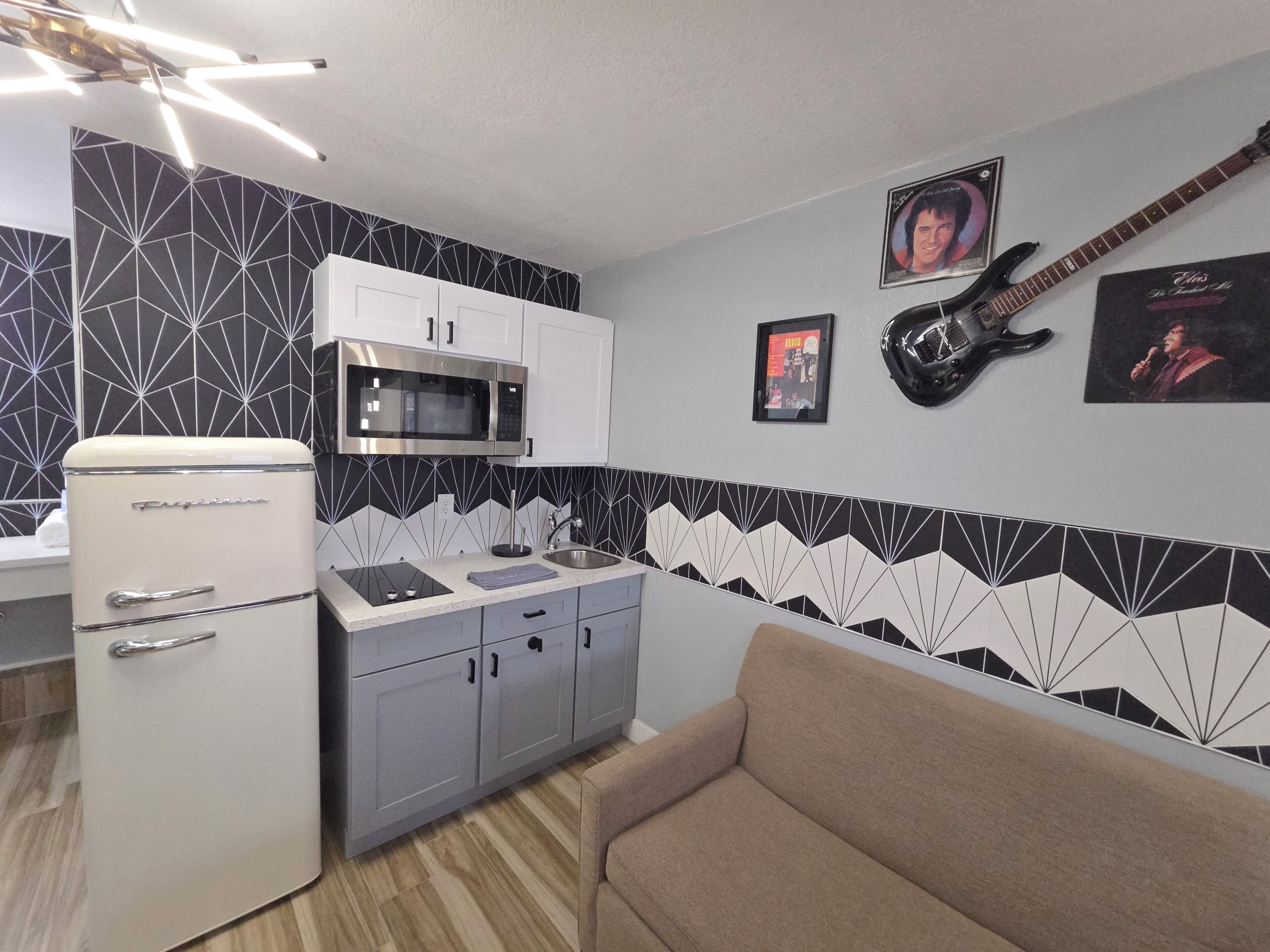 A compact kitchen with a refrigerator, microwave, and sink. There are cabinets and a sofa in the room.