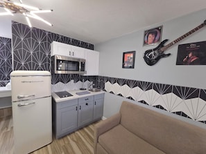 Una cocina compacta con refrigerador, microondas y lavabo. Hay armarios y un sofá en la habitación.