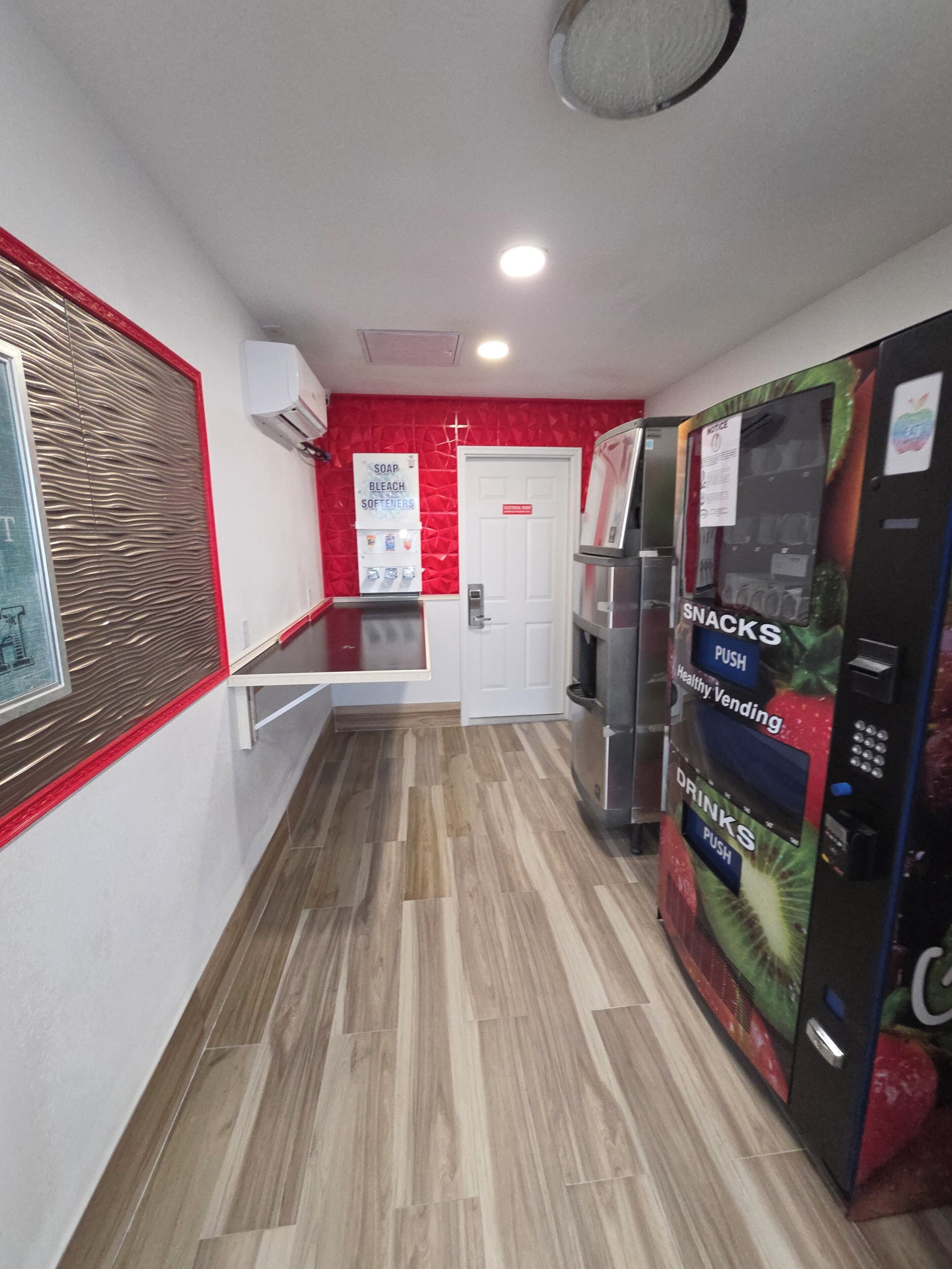 A hallway with a vending machine offering snacks and drinks, a door, and a wall-mounted air conditioner.