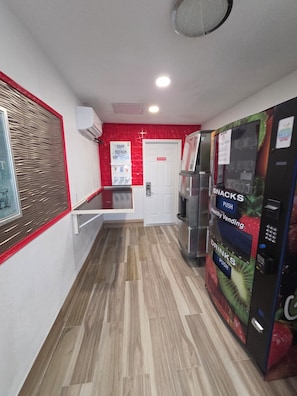 Un pasillo con una máquina expendedora que ofrece aperitivos y bebidas, una puerta y un aire acondicionado instalado en la pared.