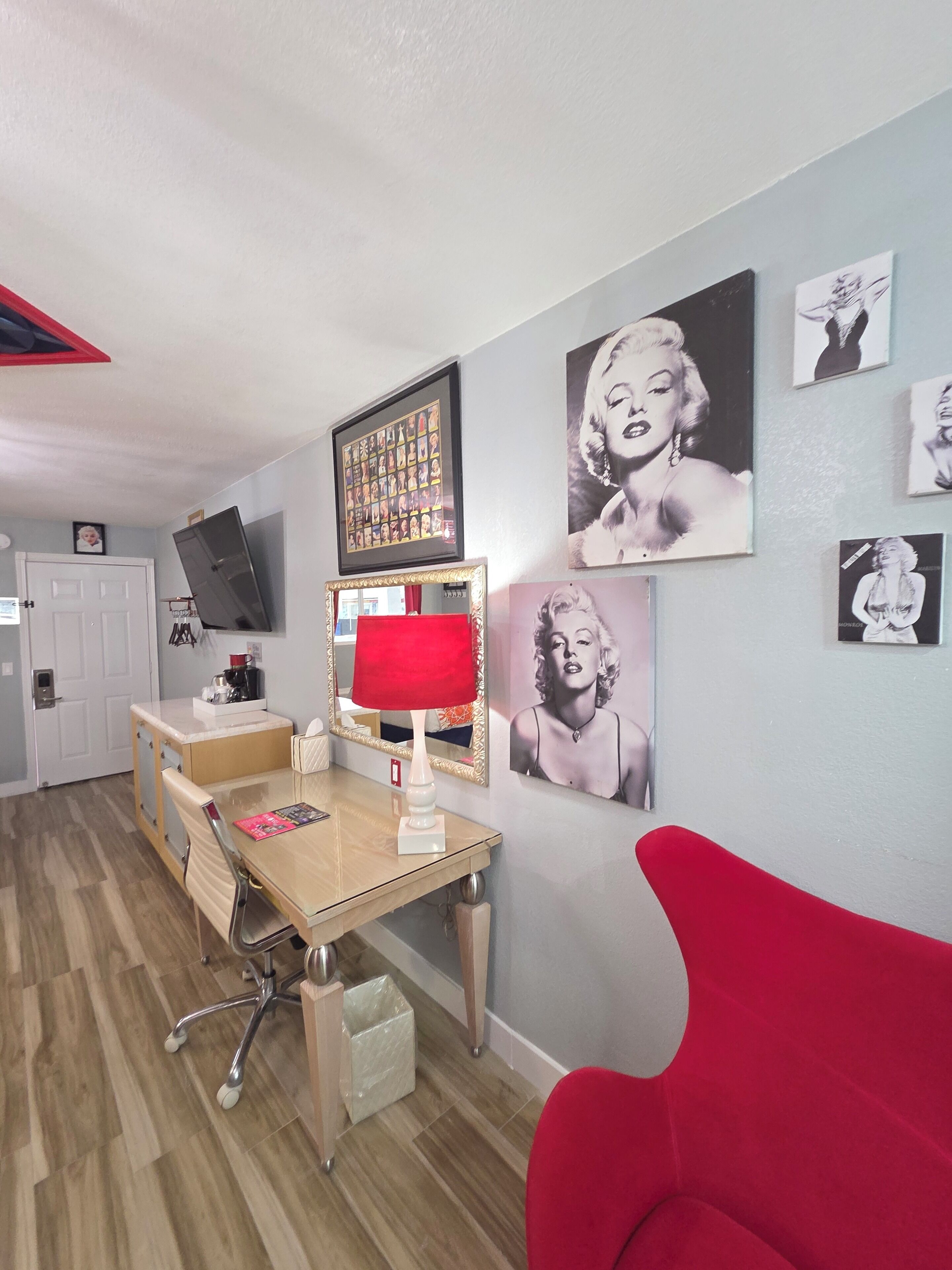 A room with a desk, chair, red lamp, and wall art.