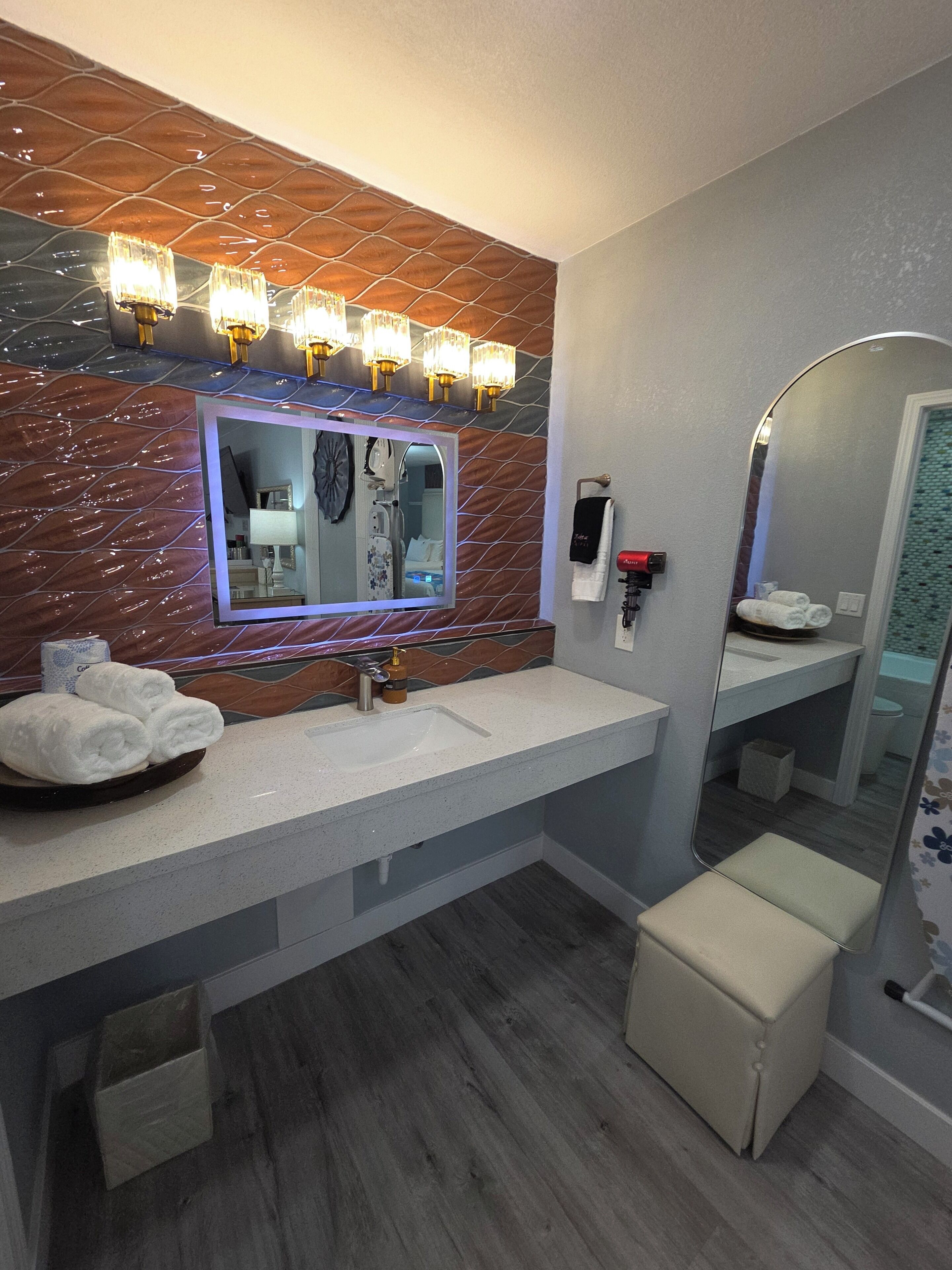 Une salle de bain moderne avec un pare-feu en marbre, un grand miroir, un meuble-lavabo et un porte-serviettes.