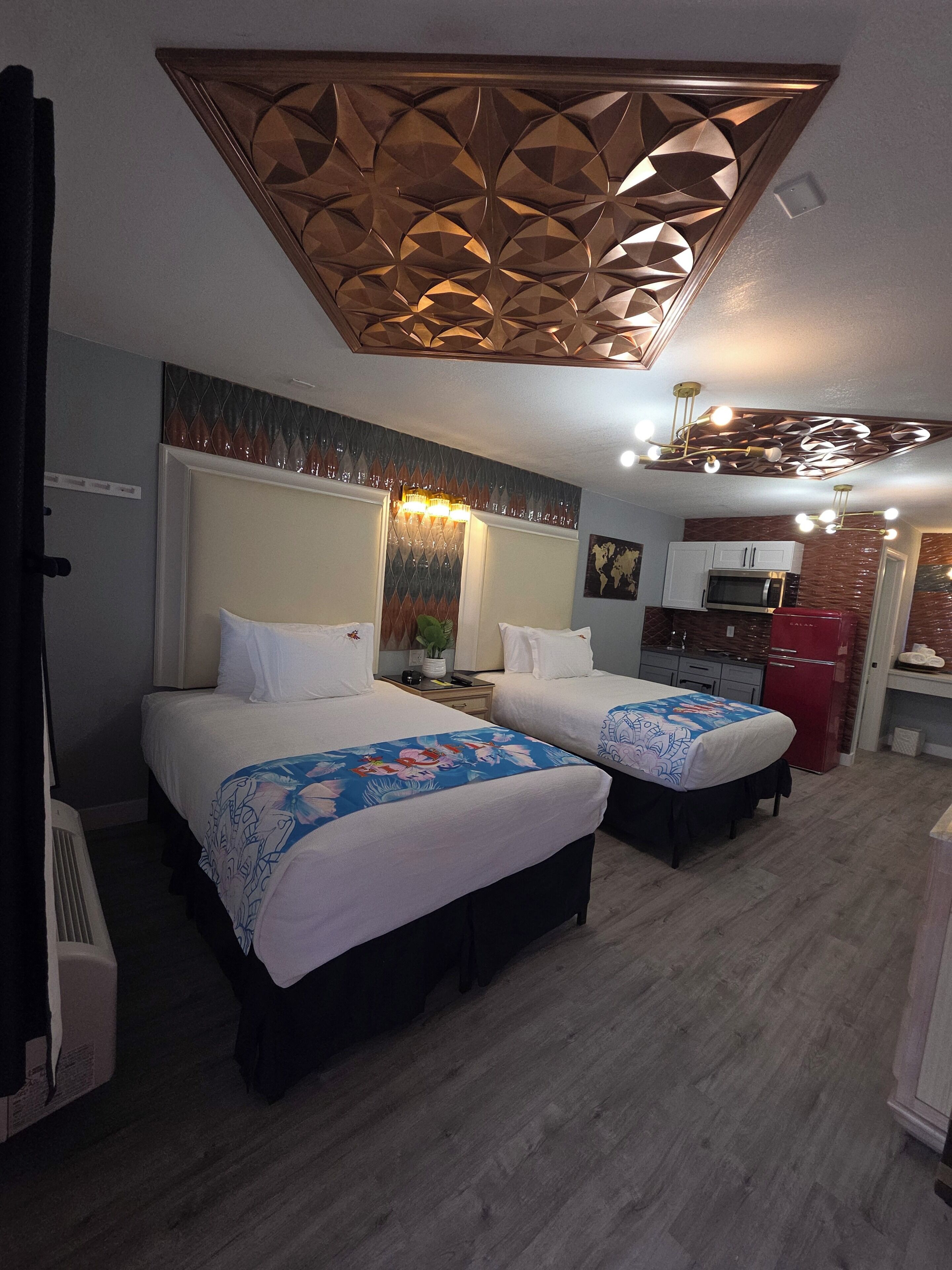 A hotel room with two beds, a kitchenette, and a decorative ceiling.