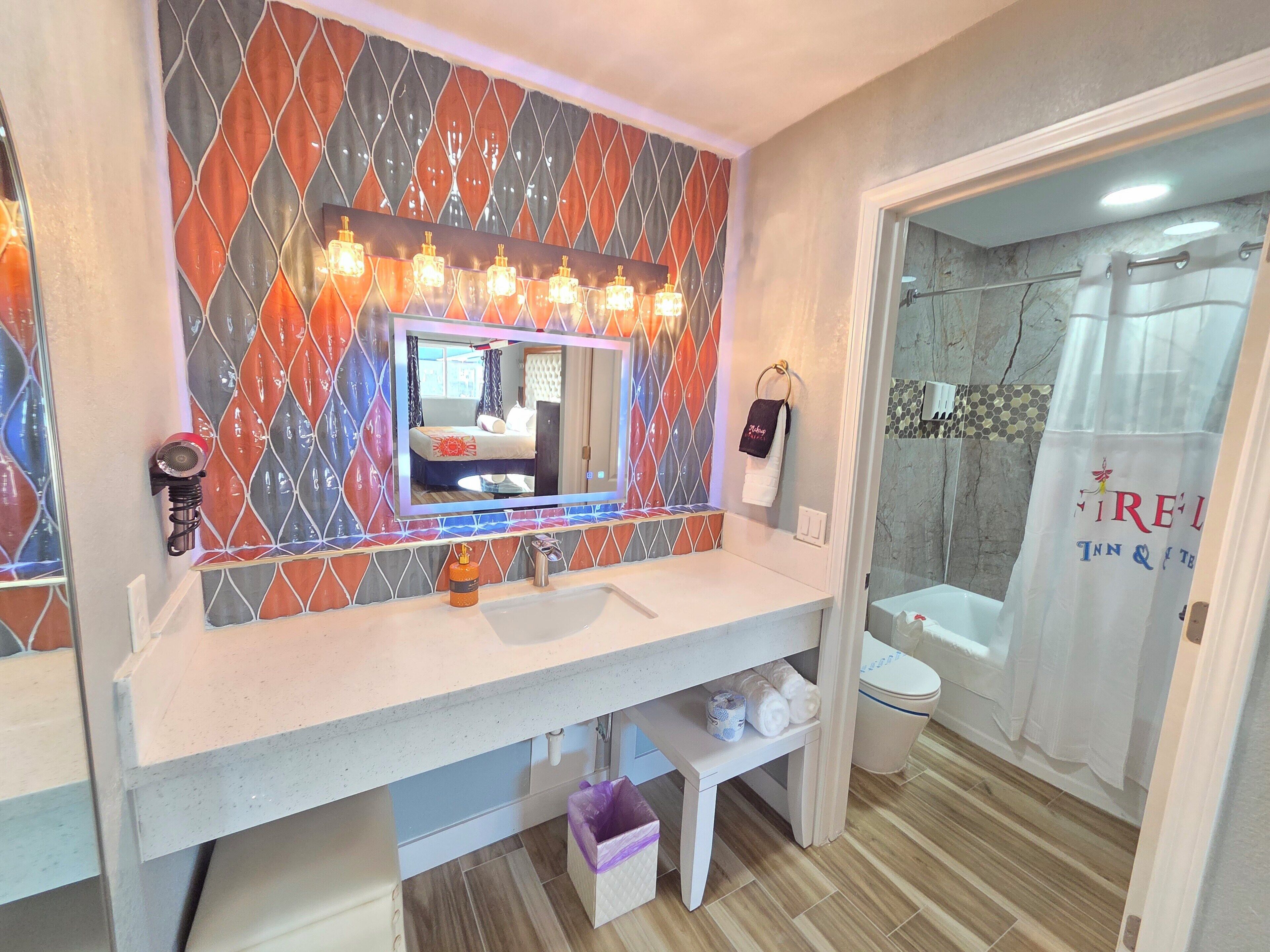 Une salle de bain avec un mur recouvert de carreaux derrière le lavabo, un miroir, un lavabo, des toilettes et un espace douche.