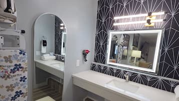 A modern bathroom with a vanity, a large mirror, and a shower area.