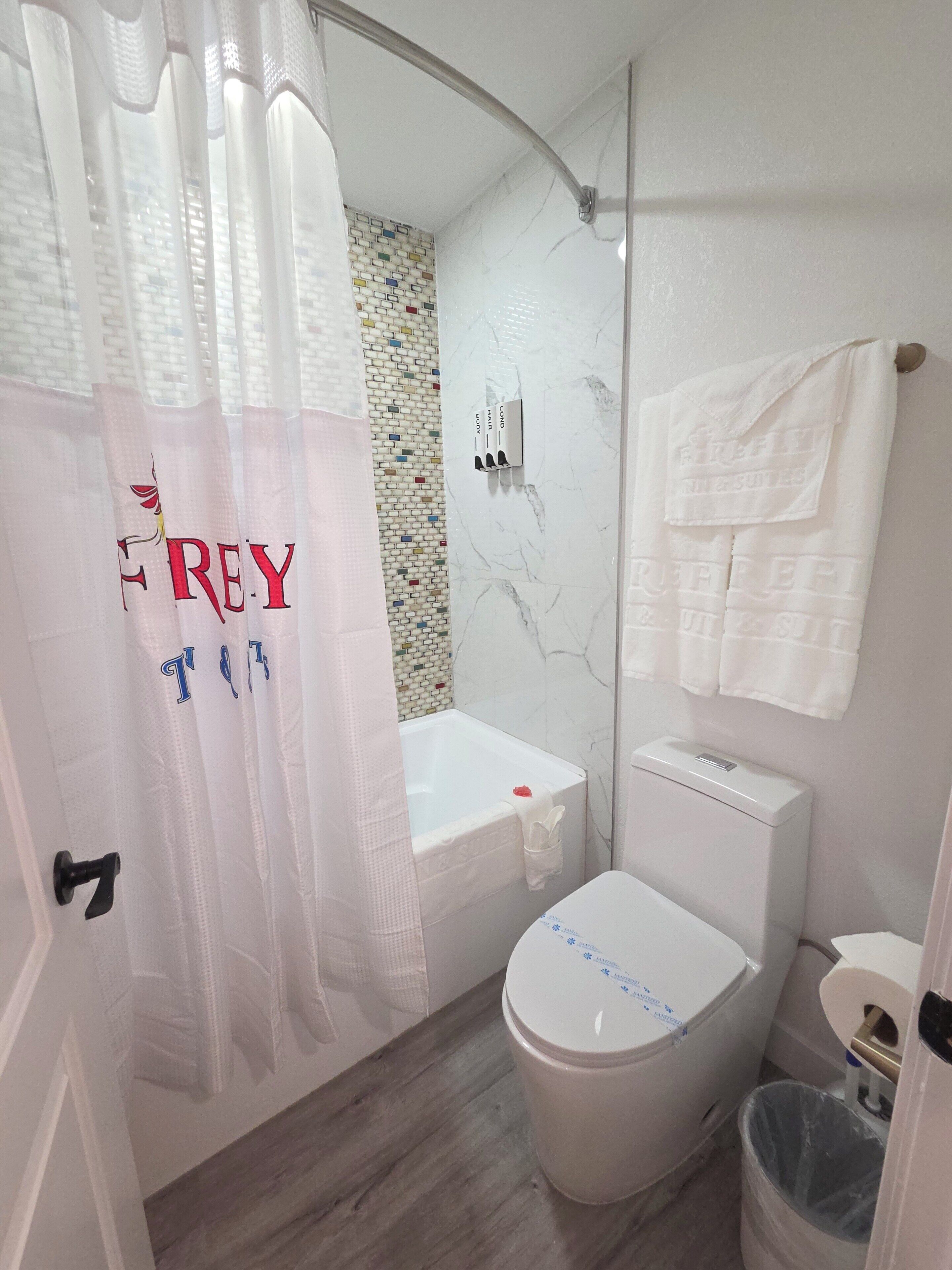 A bathroom with a shower curtain, a bathtub, a toilet, and a trash bin.