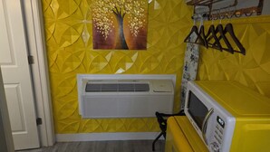 A room with a yellow geometric wall design, a white air conditioning unit, a microwave, and a wooden hanger rack.