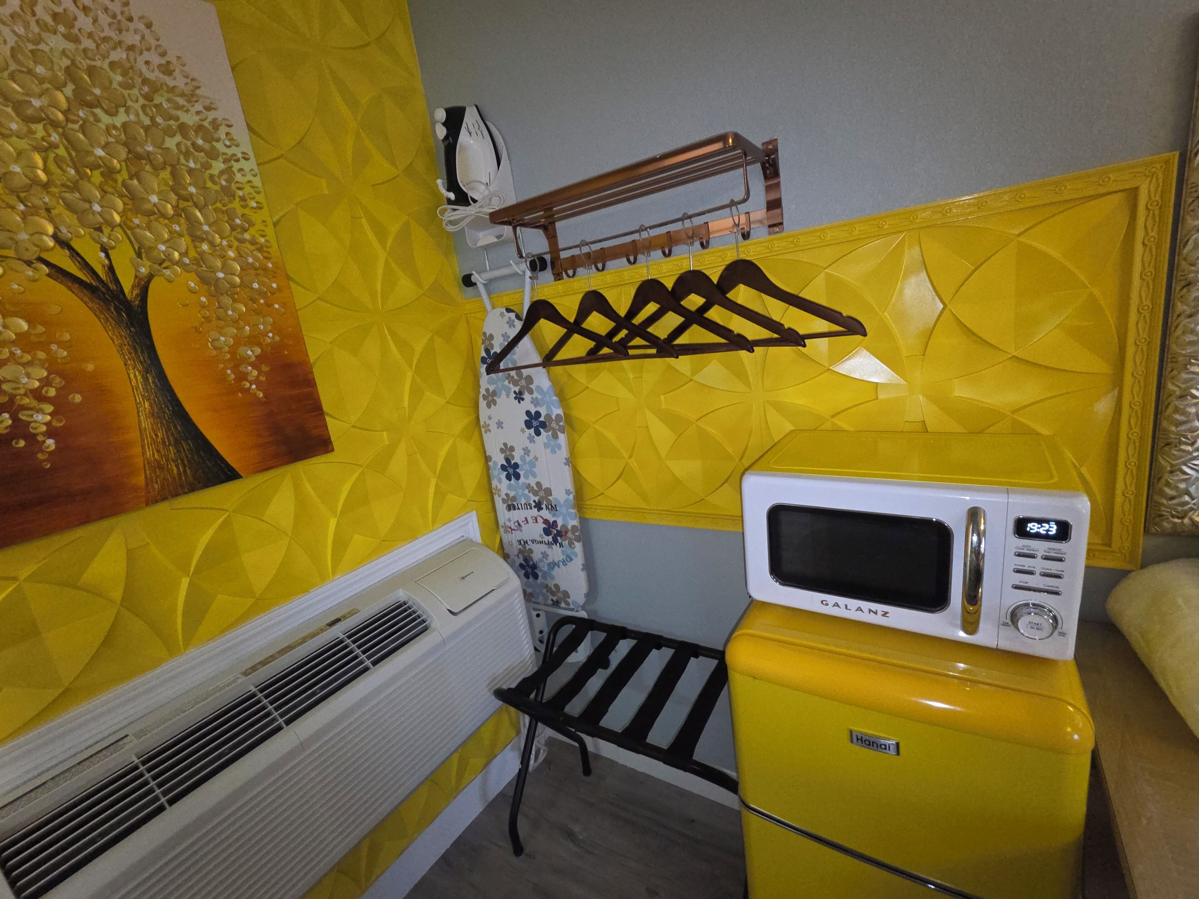 A compact kitchenette with a microwave, a small refrigerator, and a wall-mounted drying rack.