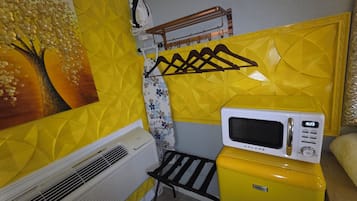 A compact kitchenette with a microwave, a small refrigerator, and a wall-mounted drying rack.
