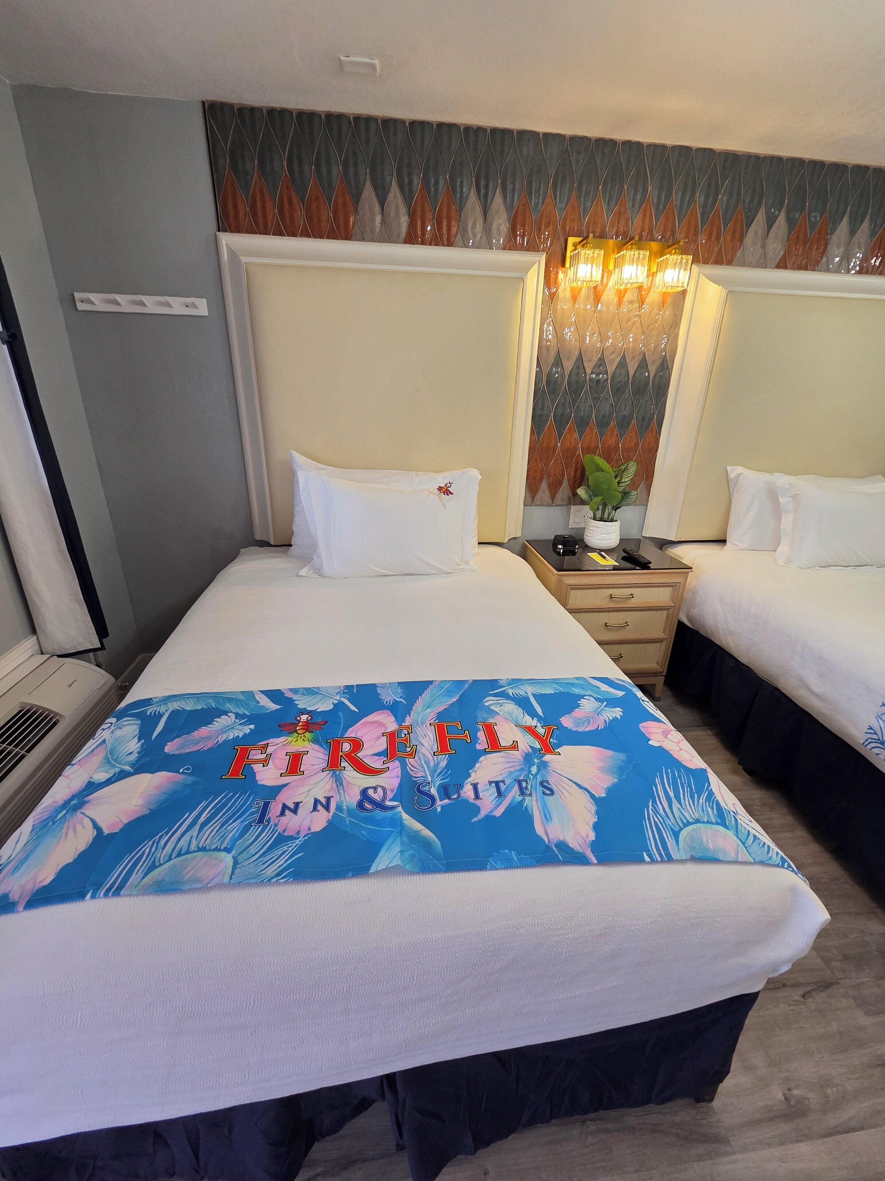A hotel room with two beds, a nightstand, a lamp, and a decorative wall panel.