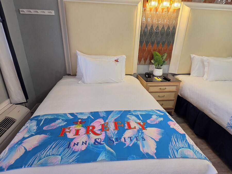 A hotel room with two beds, a nightstand, a lamp, and a decorative wall panel.