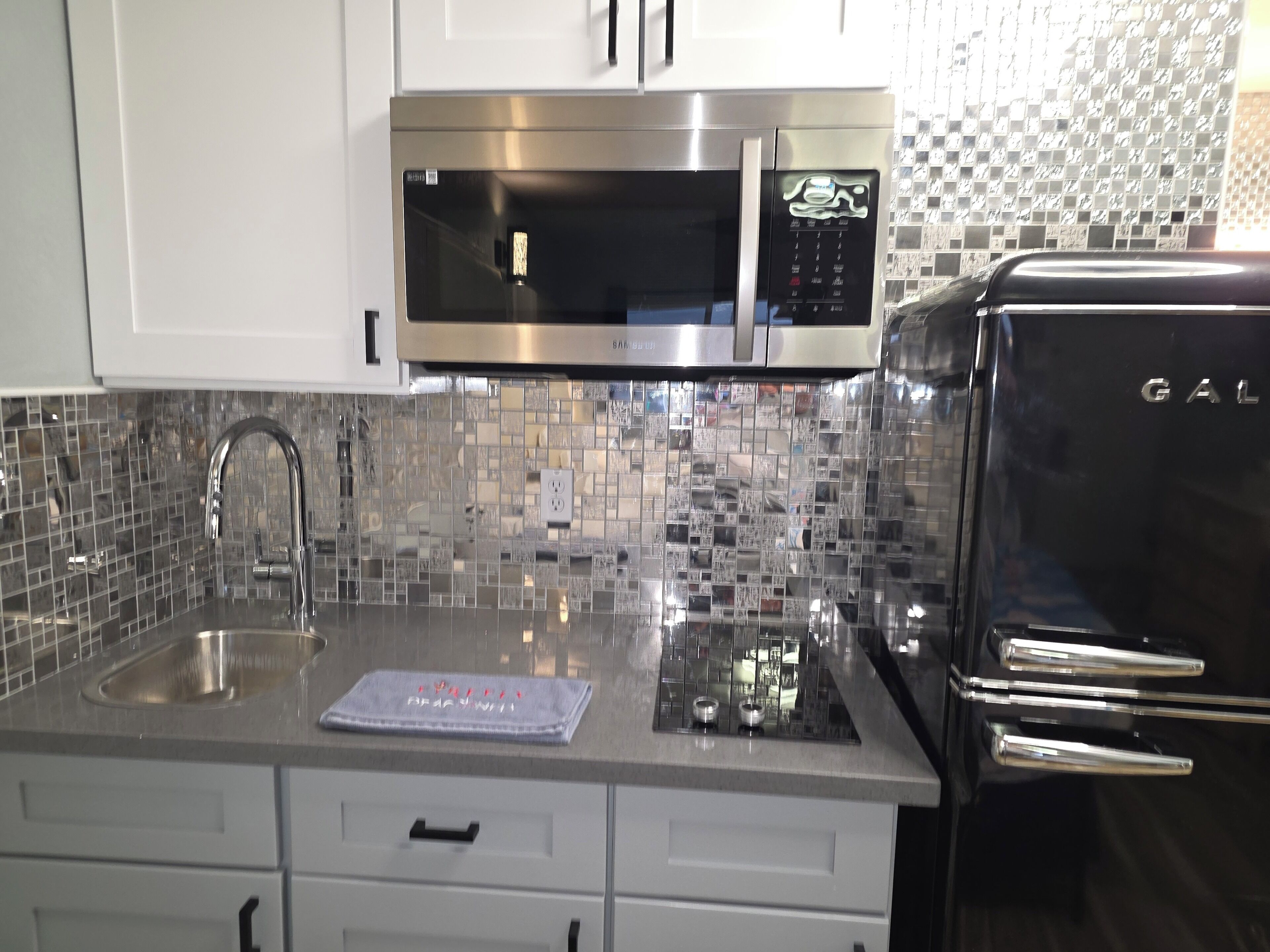 A kitchen with a stainless steel microwave, a sink, and a refrigerator.