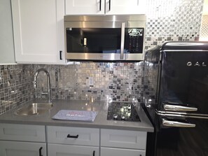 A kitchen with a stainless steel microwave, a sink, and a refrigerator. - Firefly Inn and Suites  Hastings NE (Hastings)