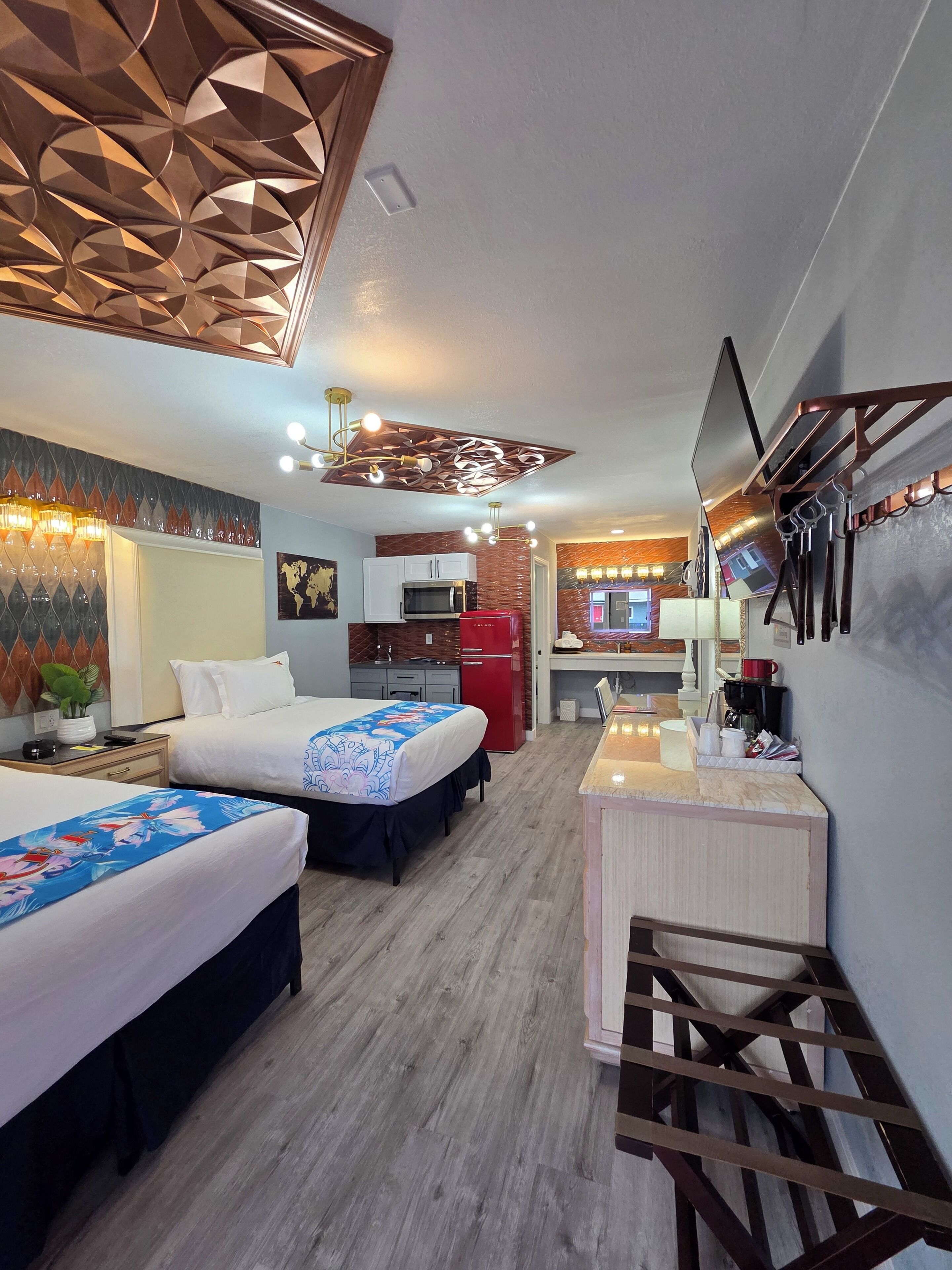 Une chambre d’hôtel avec deux lits, une kitchenette, un téléviseur fixé au mur et un plafond décoratif.