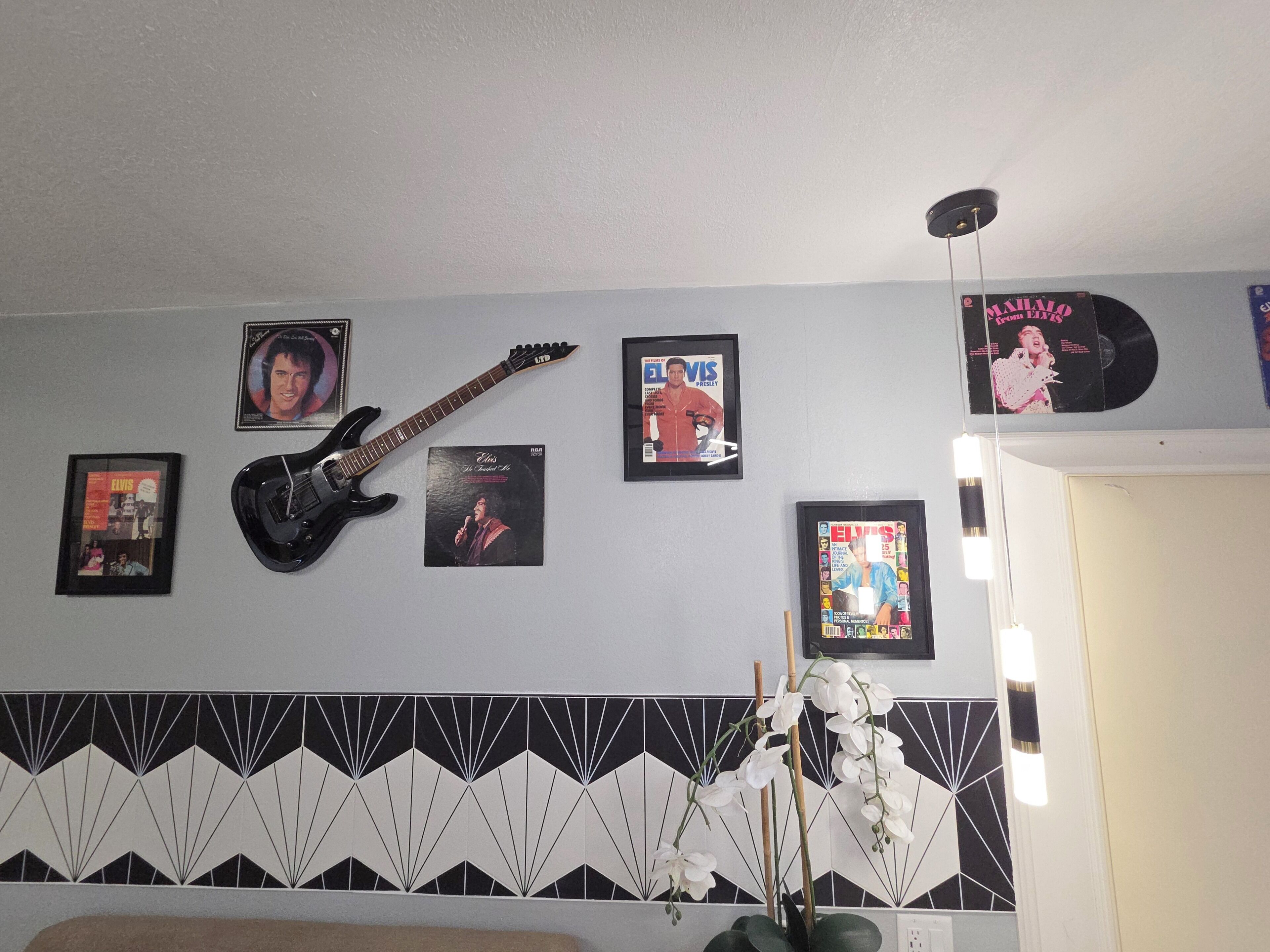 A room with a guitar, framed Elvis Presley memorabilia, and a patterned wall.
