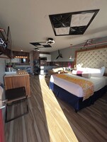 Habitación de hotel con cama, escritorio, kitchenette y ventilador de techo.