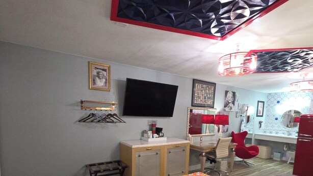 A hotel room with a bed, a desk, a chair, a television, and a red chair.
