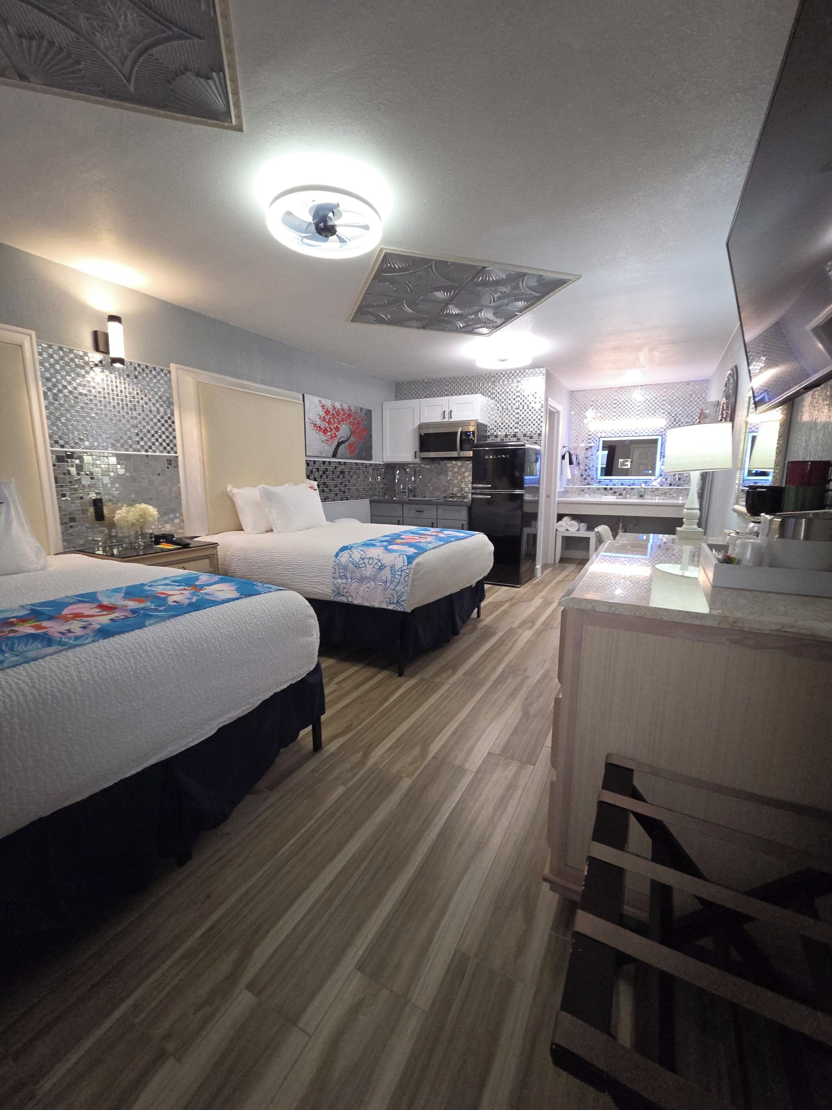 Habitación de hotel con dos camas, kitchenette, baño y escritorio.