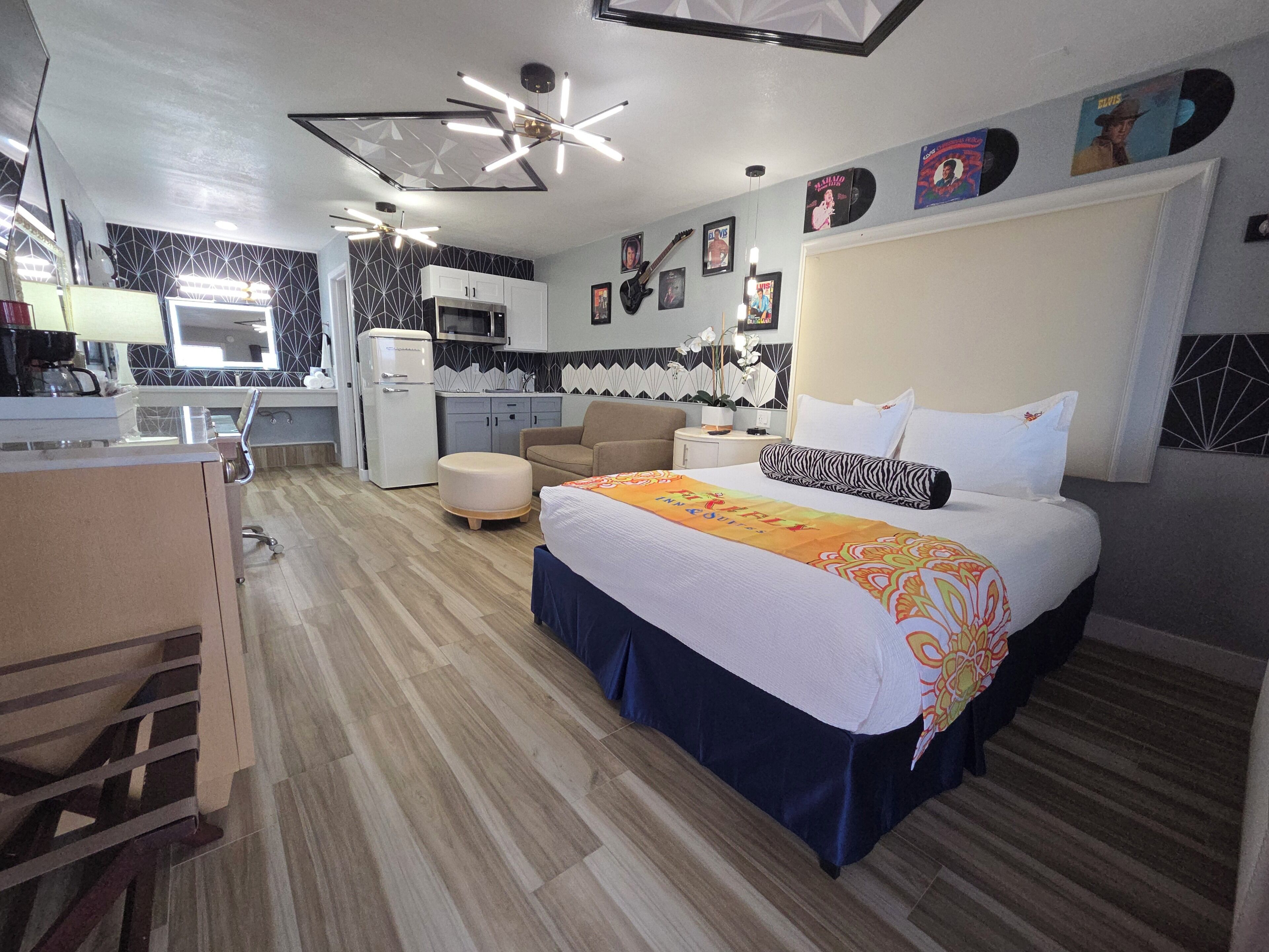 A hotel room with a bed, a desk, a kitchenette, and a ceiling fan.