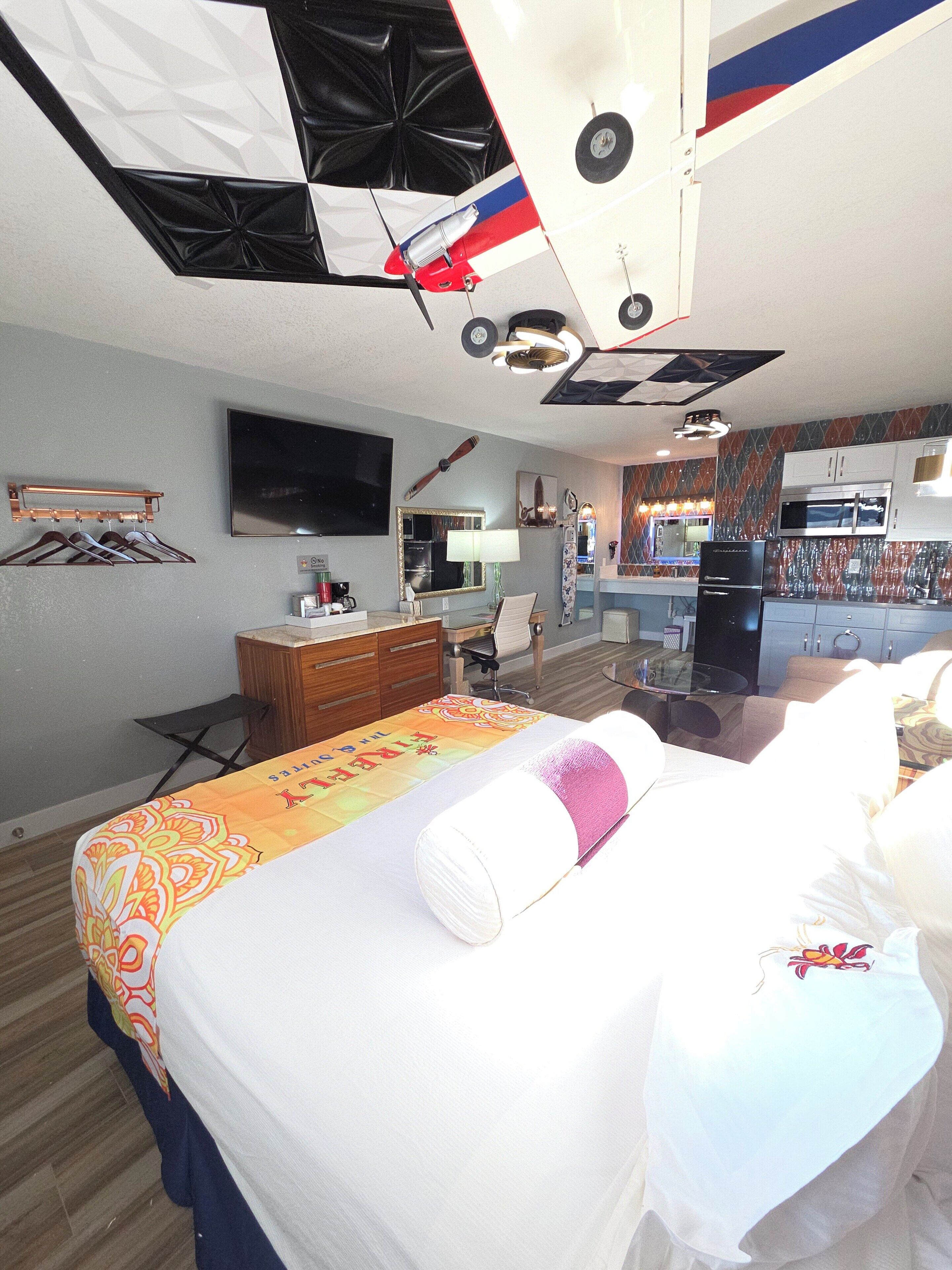 Una habitación de hotel con cama, escritorio, silla, televisor y kitchenette.