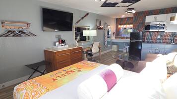 Una habitación de hotel con cama, escritorio, silla, televisor y kitchenette.