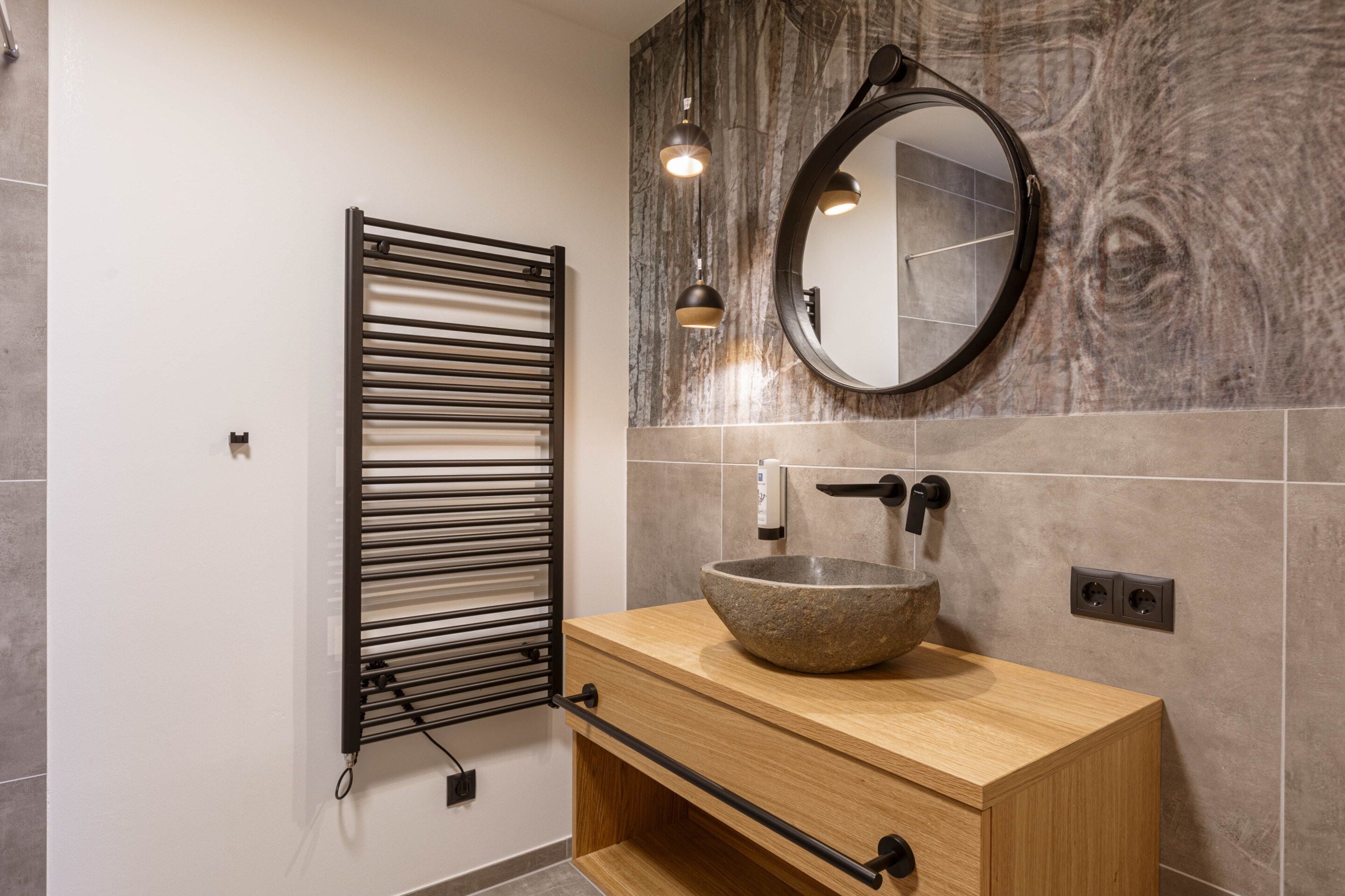 Une salle de bain avec un meuble-lavabo en bois, un miroir rond, un porte-serviettes et un lavabo en pierre.