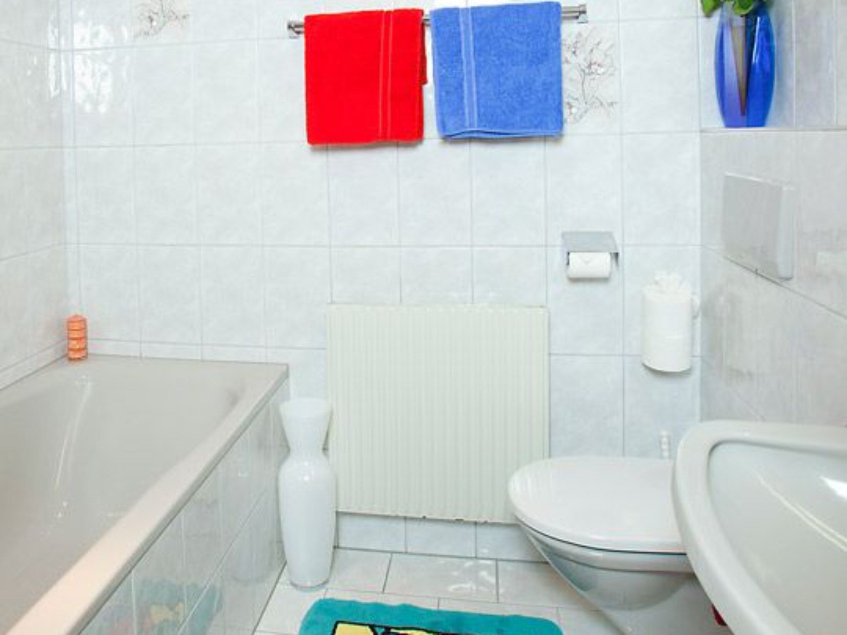 A bathroom with a bathtub, toilet, and a towel rack with red and blue towels.