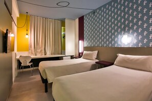 Ein Hotelzimmer mit zwei Betten, einem Schreibtisch, einem Stuhl und einem fensterbepflanzten Fenster.