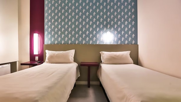 Una habitación de hotel con dos camas individuales, una mesita de noche con lámpara y una pared decorada con motivos de cactus.