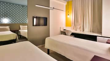 Quarto de hotel com duas camas, televisão, escrivaninha e janela com cortinas.