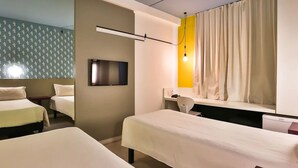 Habitación de hotel con dos camas, televisor, escritorio y ventana con cortinas.