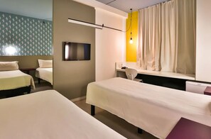 Ein Hotelzimmer mit zwei Betten, einem Fernseher, einem Schreibtisch und einem Fenster mit Vorhängen.