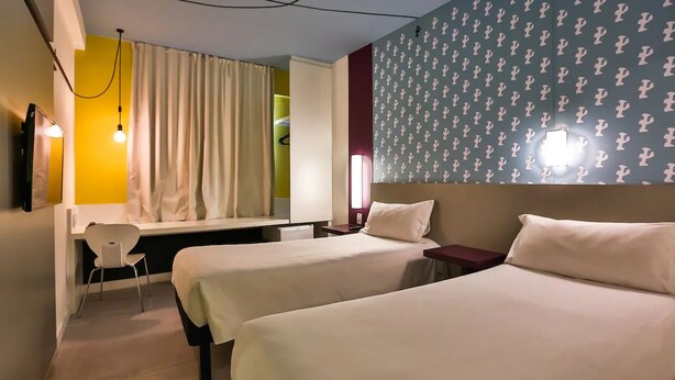 Habitación de hotel con dos camas, un escritorio, una silla y una ventana con cortinas.