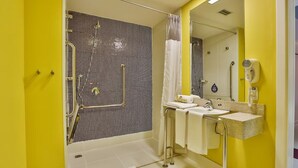 Un baño con pared amarilla, ducha con puerta de cristal, lavabo con espejo y secador de pelo en la pared.