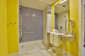 Un baño con pared amarilla, ducha con puerta de cristal, lavabo con espejo y secador de pelo en la pared.